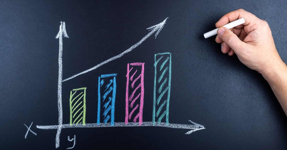 A man's hand with chalk draws an economic growth graph on a chalkboard
